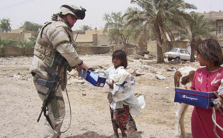 A Soldier with the 256th Brigade hands out supplies to local children during a patrol in Iraq, Jan. 3, 2004. In addition to combat operations, the Louisiana National Guard brigade, then a mechanized infantry unit, supported humanitarian and civil affairs efforts during Operation Iraqi Freedom III. U.S. Army National Guard courtesy photo