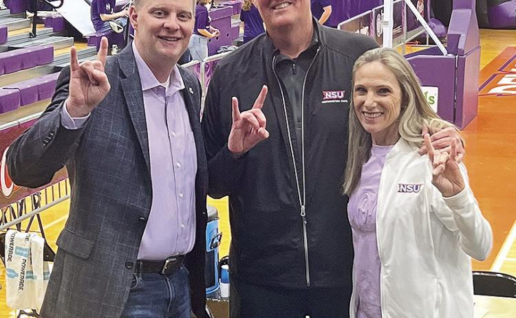 Alumni Eric (center) and Marylalyce Walsh Cox (right) pose with Northwestern State Director of Athletics Kevin Bostian during a Northwestern State basketball game. Submitted photo.