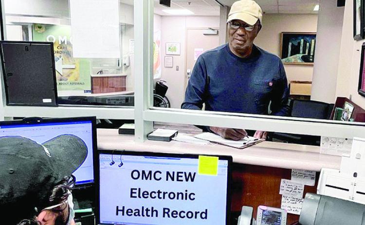 OMC Patient Services Representative Jordan Mulso (seated) assists OMC Board Member Melvin Holmes with checking into his appointment.
