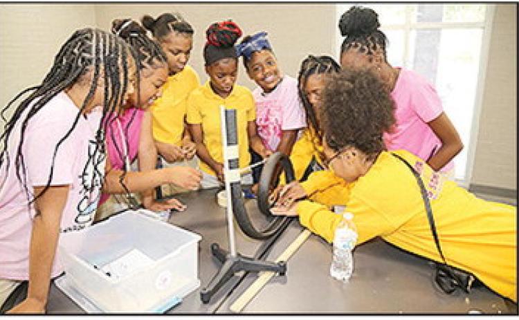 Pictured are Natchitoches Jr. High students Aretha Potter, Zariah Pearrie, Janiah Heard, Lyric Thomas, Mariah Robinson, Harmony Remo, Ja’Kiera Humphrey and Jenissy Robinson participating in the “Factory Physics Challenge.” The all-female team of sixth and seventh graders won the competition for being the first to successfully design a gravity- powered factory line that delivered a marble into a cup using pipe insulation, tape and binder clips.
